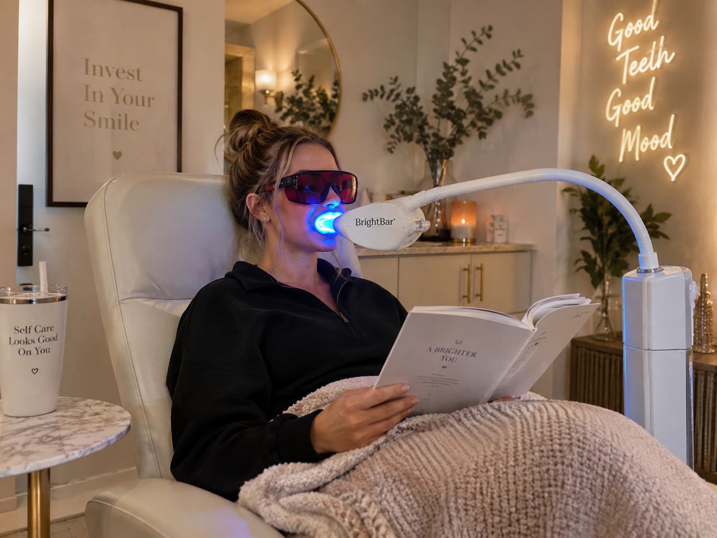 Guest relaxing with a book and a cozy blanket under the whitening light during a 60-minute teeth whitening session at Bright Now in Prescott, AZ